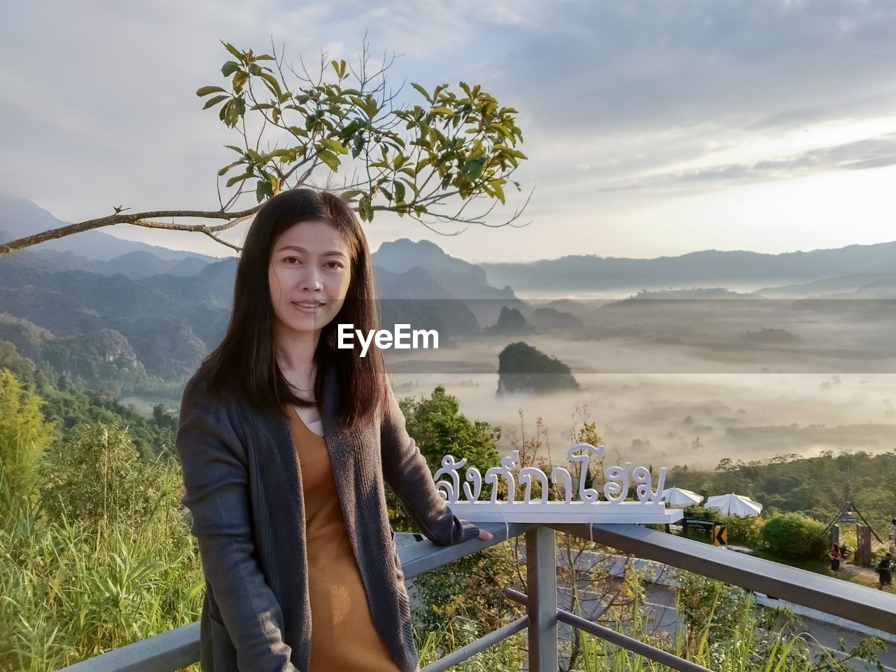 Portrait of smiling woman standing by railing on mountain against sky