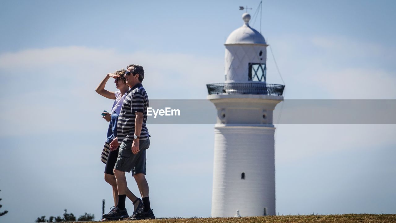 LOW ANGLE VIEW OF YOUNG MAN STANDING AGAINST LIGHTHOUSE