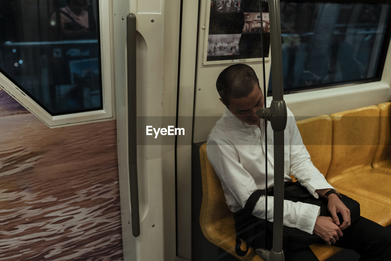 Man with bag sleeping while sitting in train