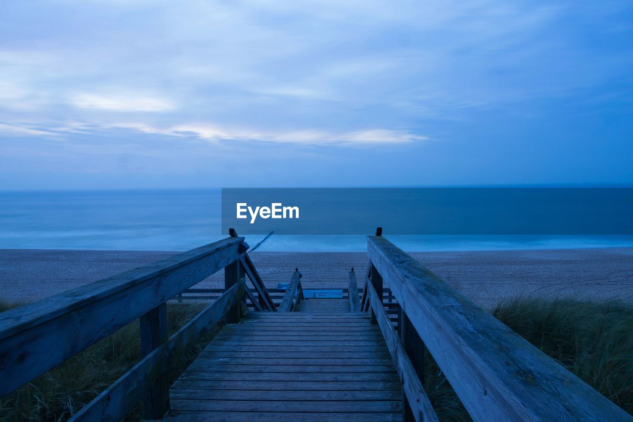 Empty wooden pier on sea against sky