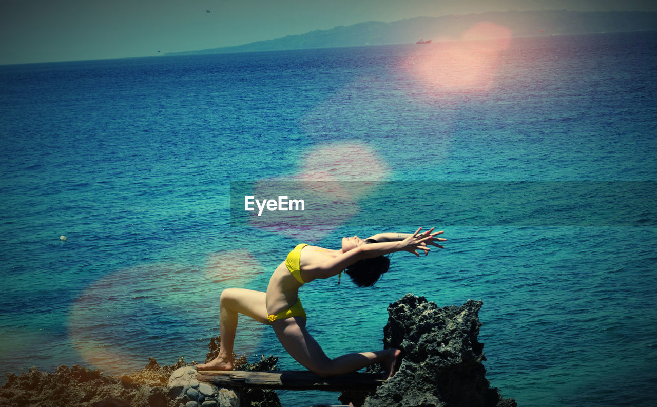 Full length of woman exercising against sea on sunny day