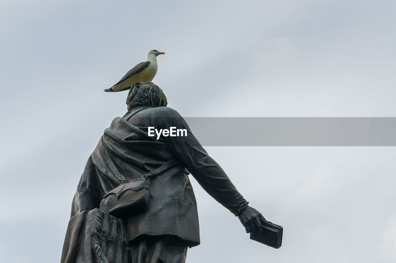 LOW ANGLE VIEW OF STATUE OF BIRD PERCHING ON SCULPTURE AGAINST SKY