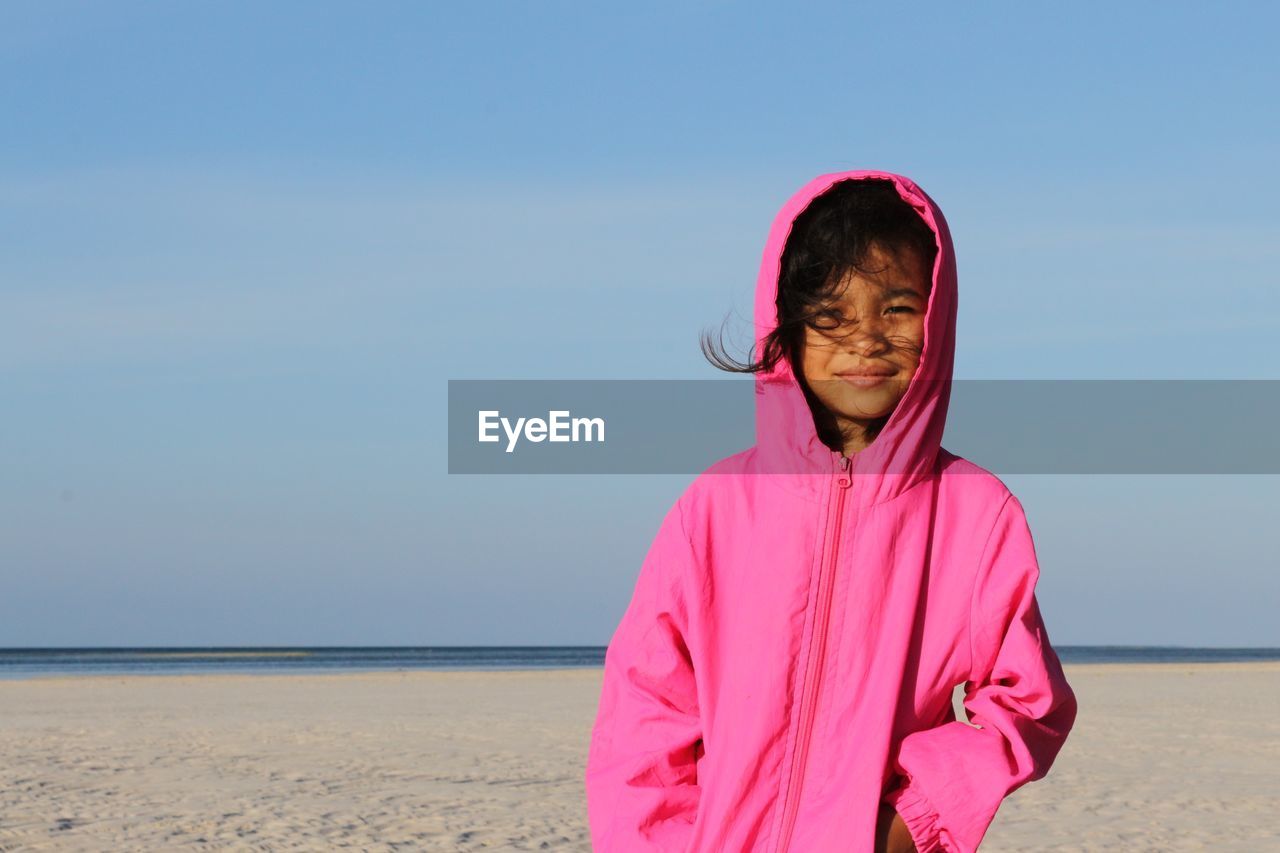 Portrait of young woman standing at beach against clear sky