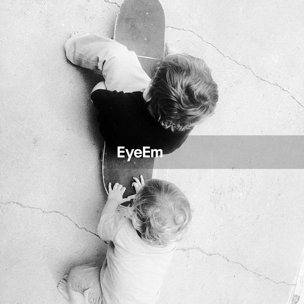 High angle view of baby boy pushing brother sitting on skateboard