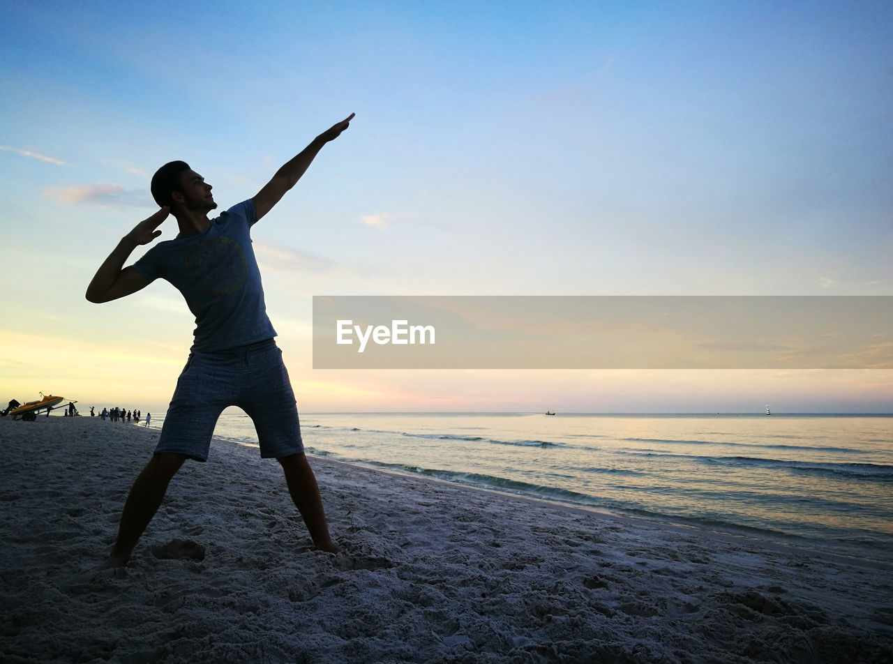 Man posing against sea during sunset