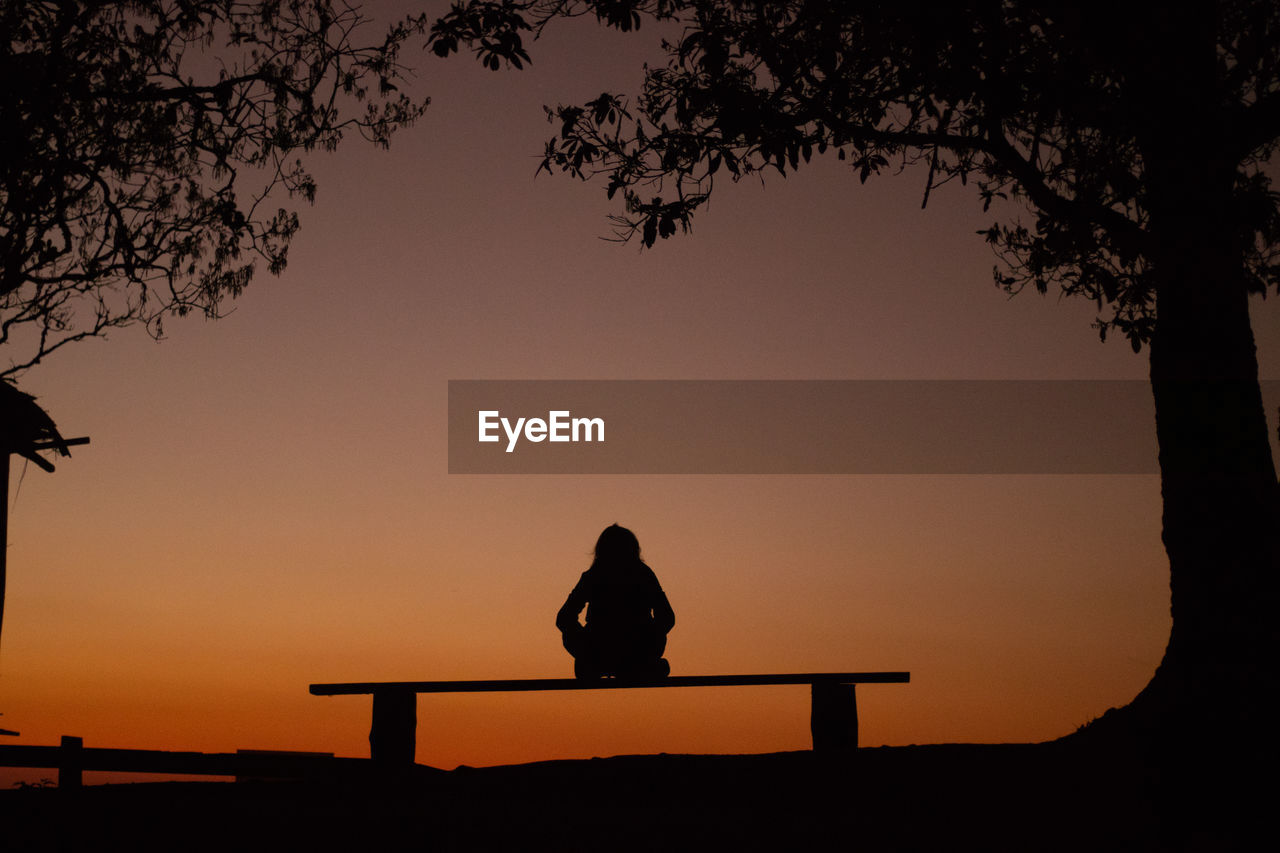 SILHOUETTE WOMAN SITTING ON BENCH AT SUNSET