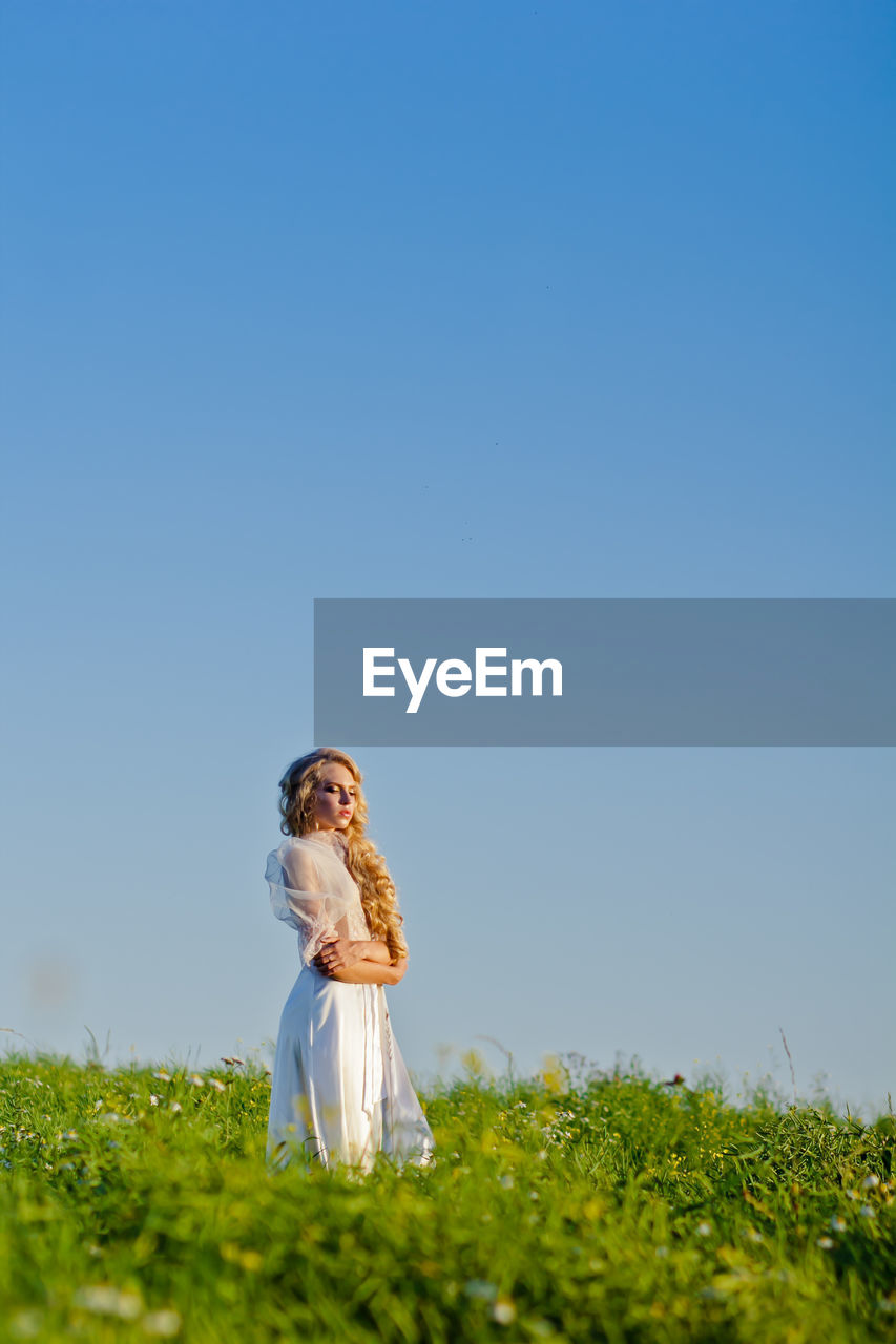 Young woman standing on field against clear blue sky