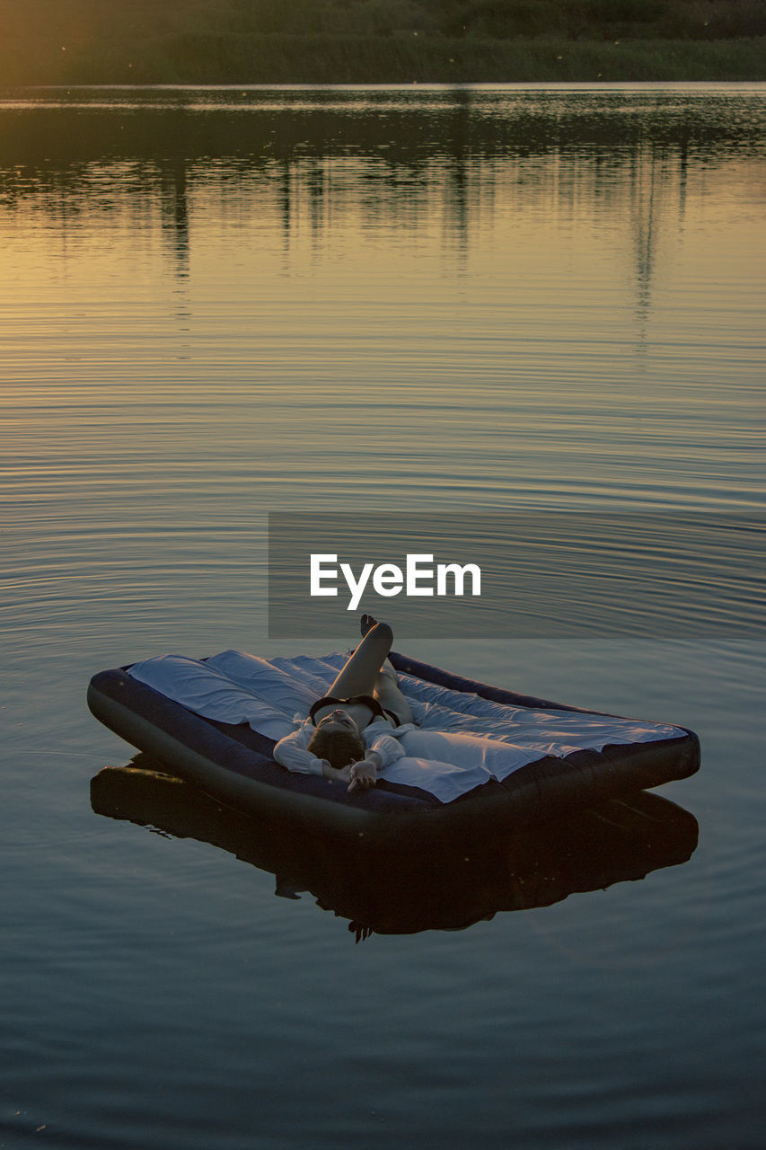 Young woman lies on a mattress on the water during sunset