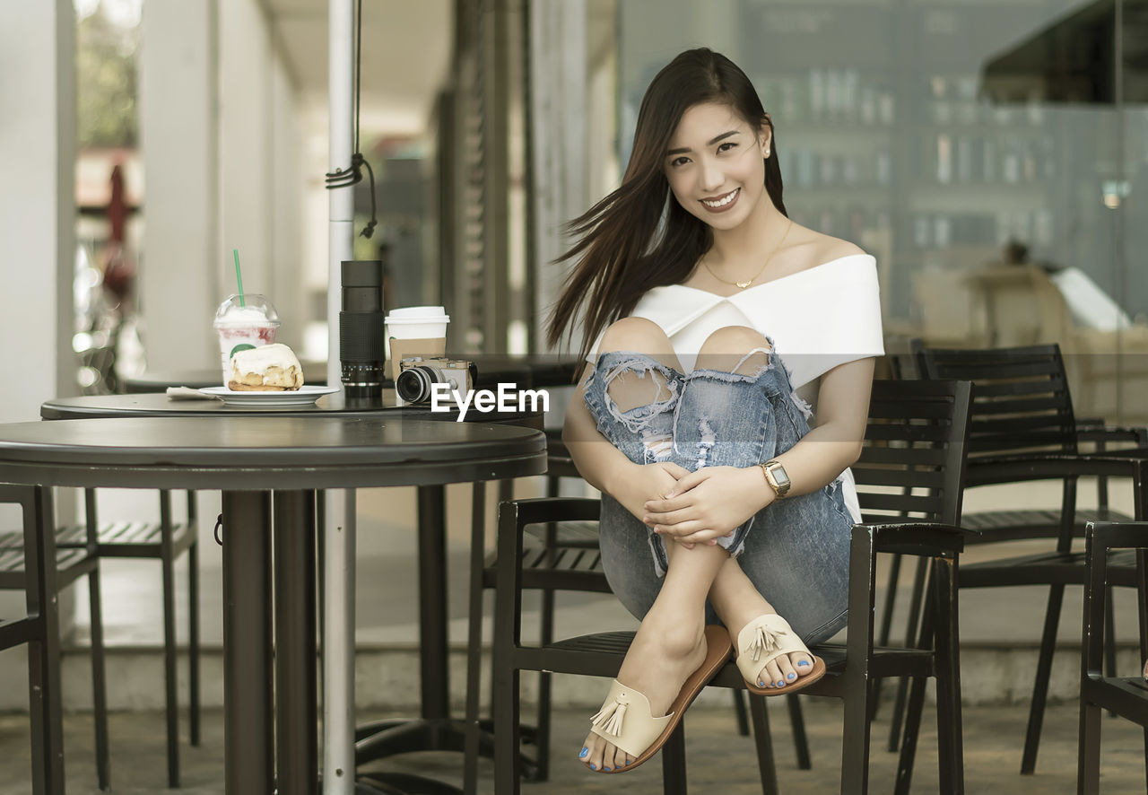 Full length portrait of smiling young woman sitting on chair