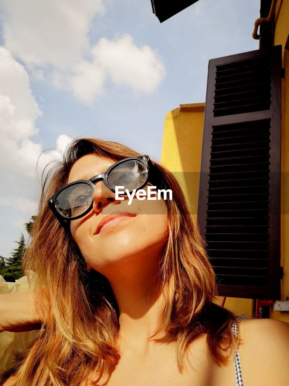 Smiling young woman wearing sunglasses against sky during sunny day