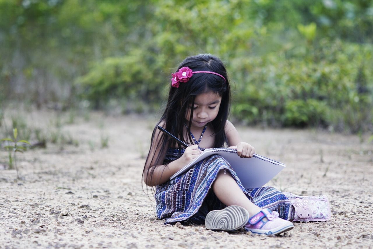 Full length of cute girl writing on book at field