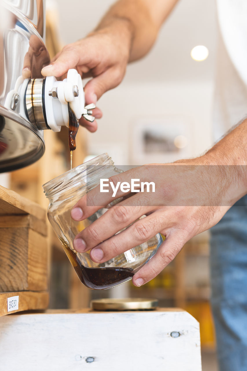 Male entrepreneur pouring honey in jar at shop