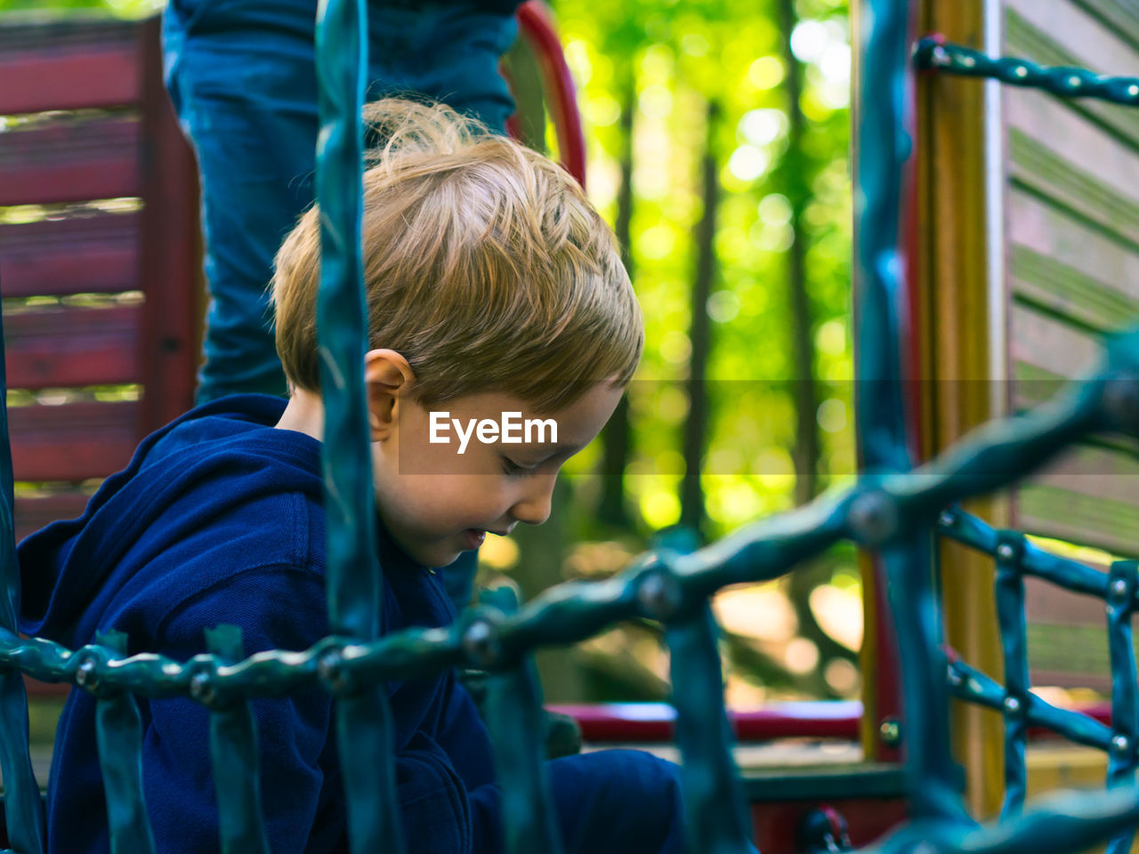 REAR VIEW OF BOY LOOKING AT PLAYGROUND EQUIPMENT