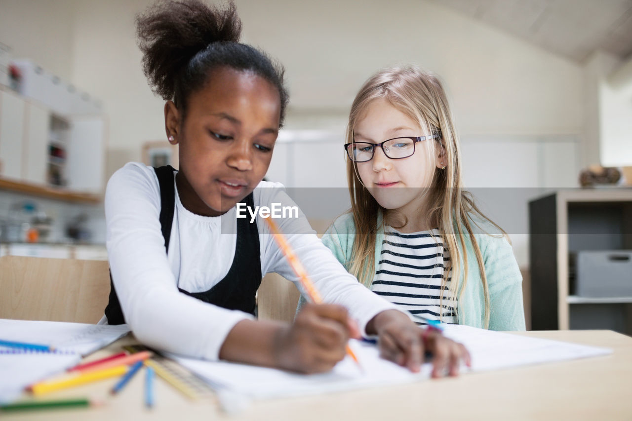 Girl assisting friend while studying in classroom at school