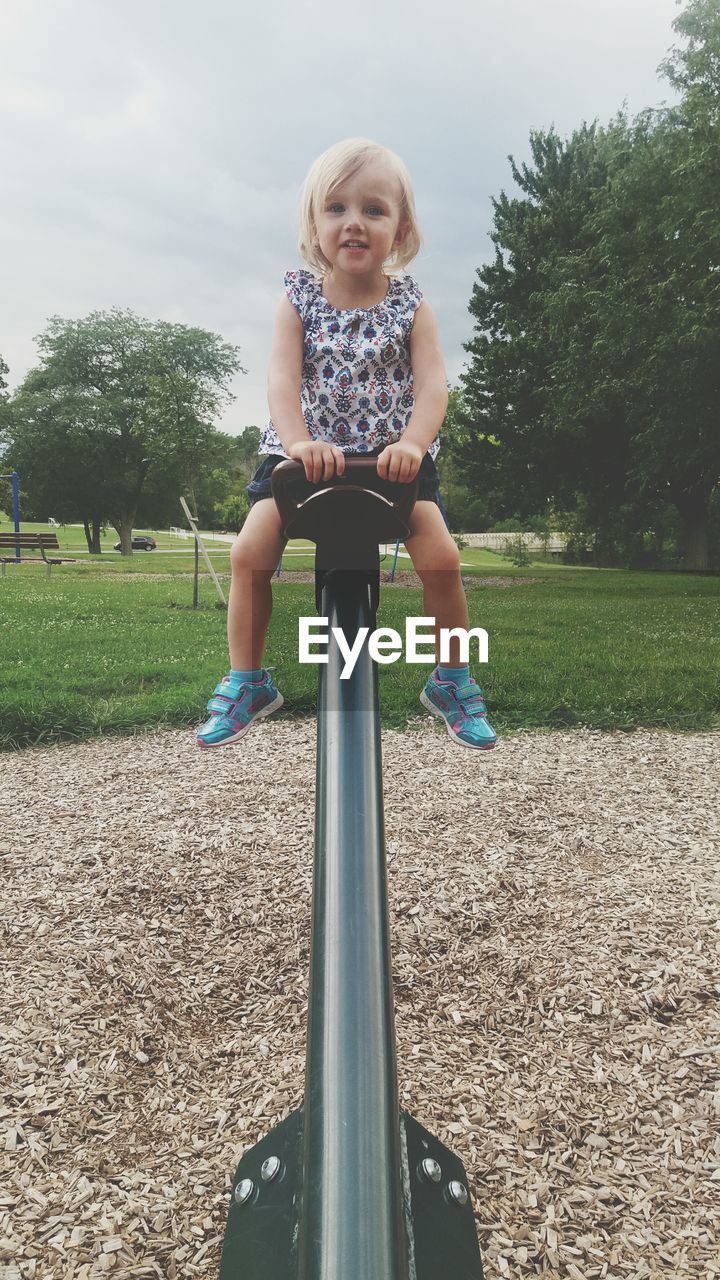 Portrait of girl sitting on seesaw at playground