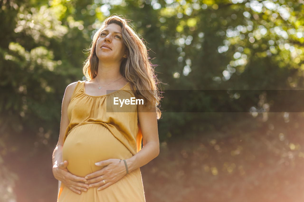 Low angle view of pregnant woman with hands on stomach standing in park