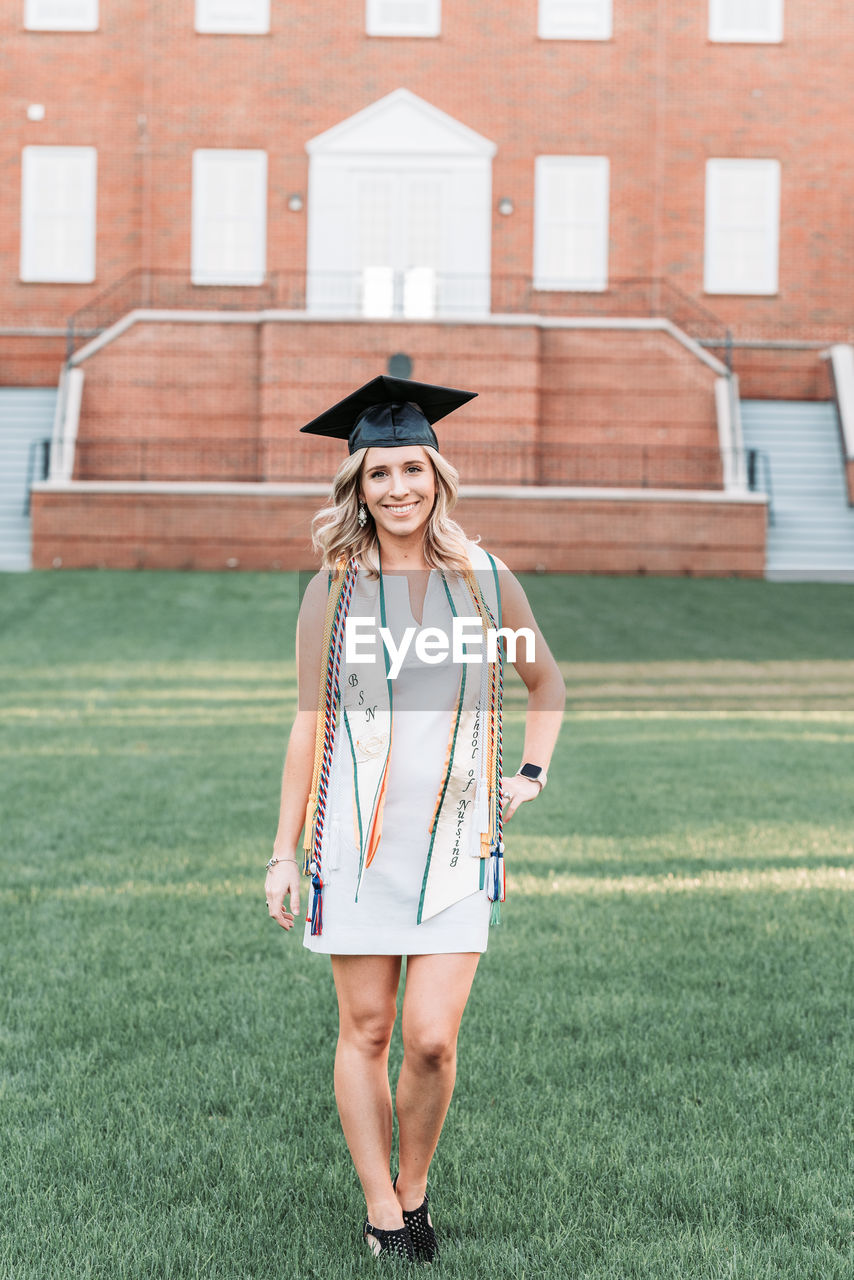 PORTRAIT OF A SMILING YOUNG WOMAN STANDING AGAINST BUILT STRUCTURE