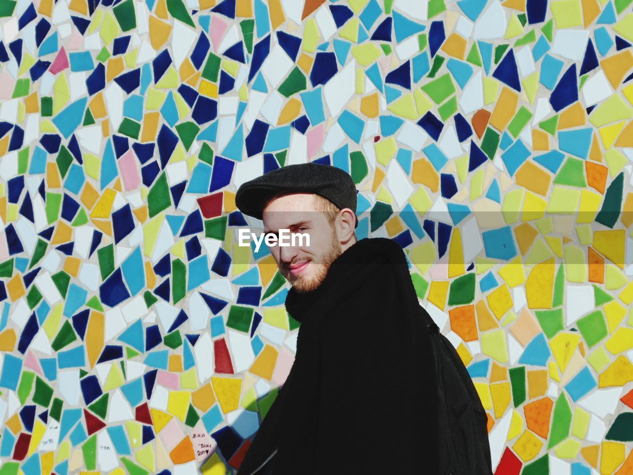 Portrait of smiling young man standing against colorful mosaic wall