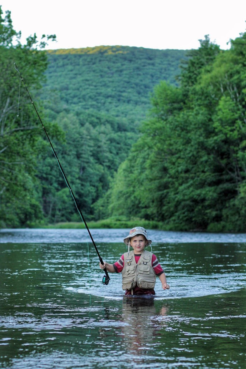 MAN FISHING IN LAKE AGAINST TREES