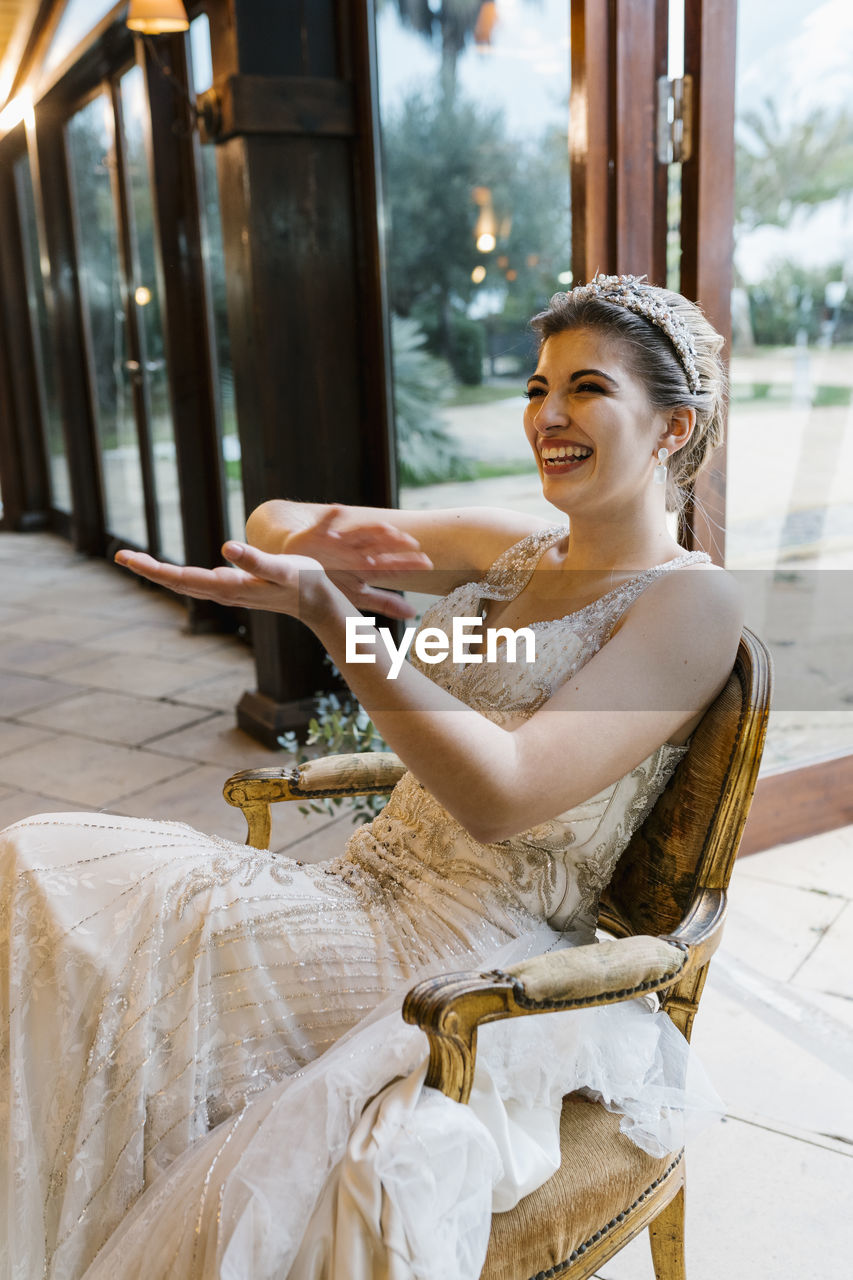 Happy bride clapping hands while sitting on chair at banquet