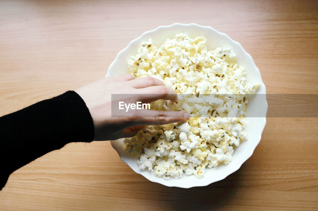 Cropped hand having popcorn on table