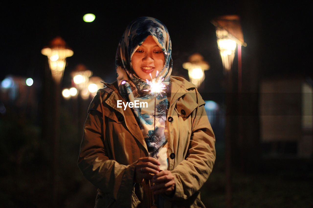 Woman holding sparkler at night