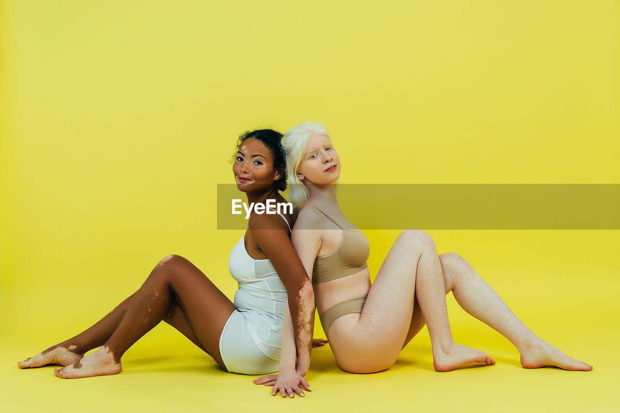 Side view of young women sitting against yellow background