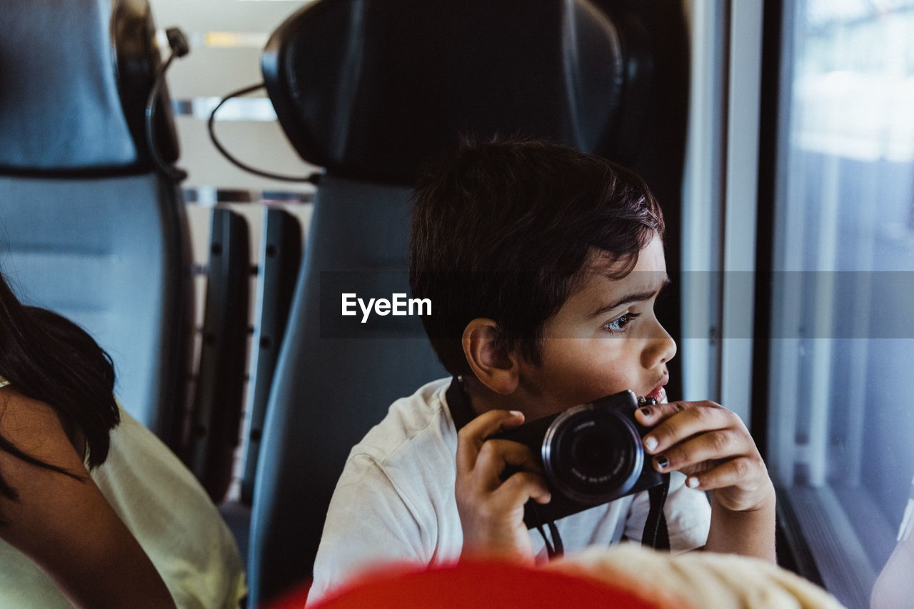 Curious boy with camera looking at window while sitting in train