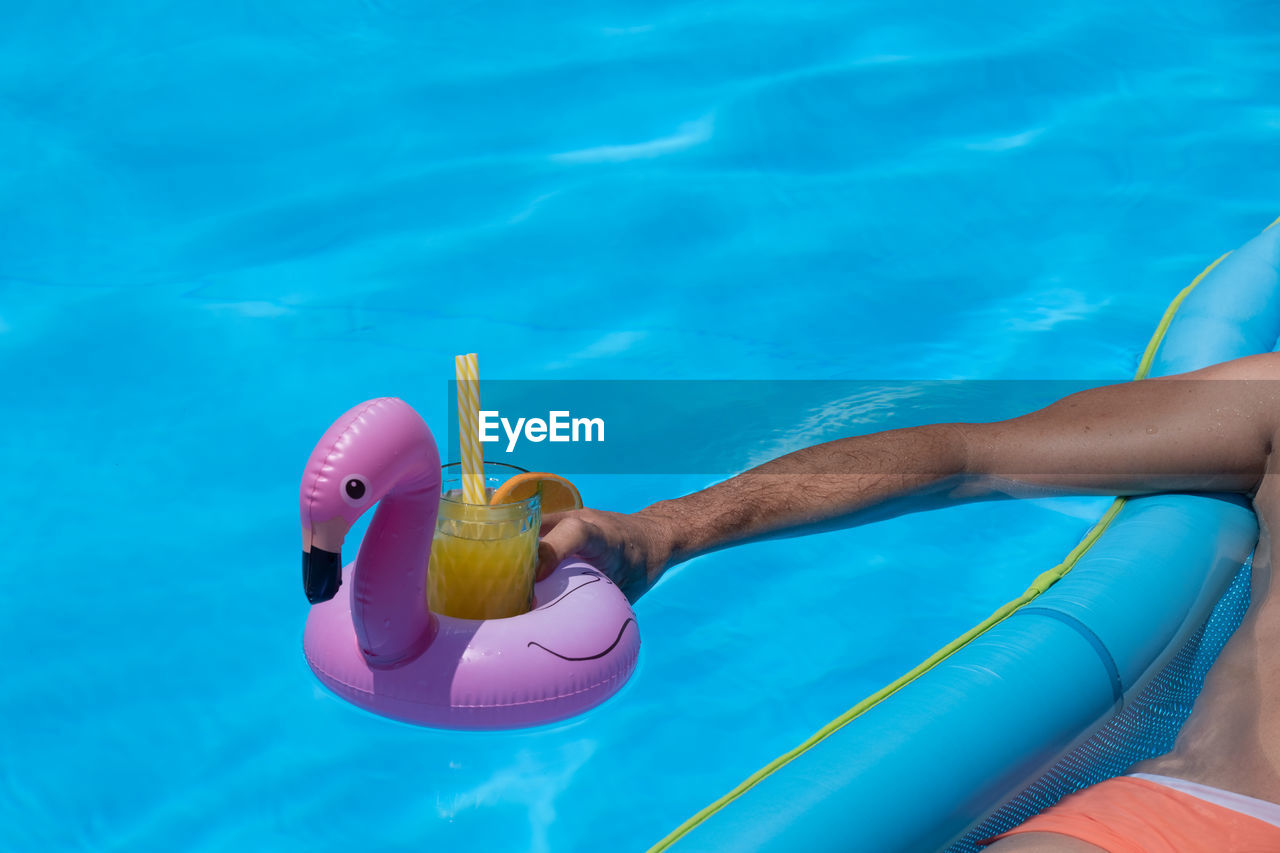 Man on air mattress in swimming pool holding a drink