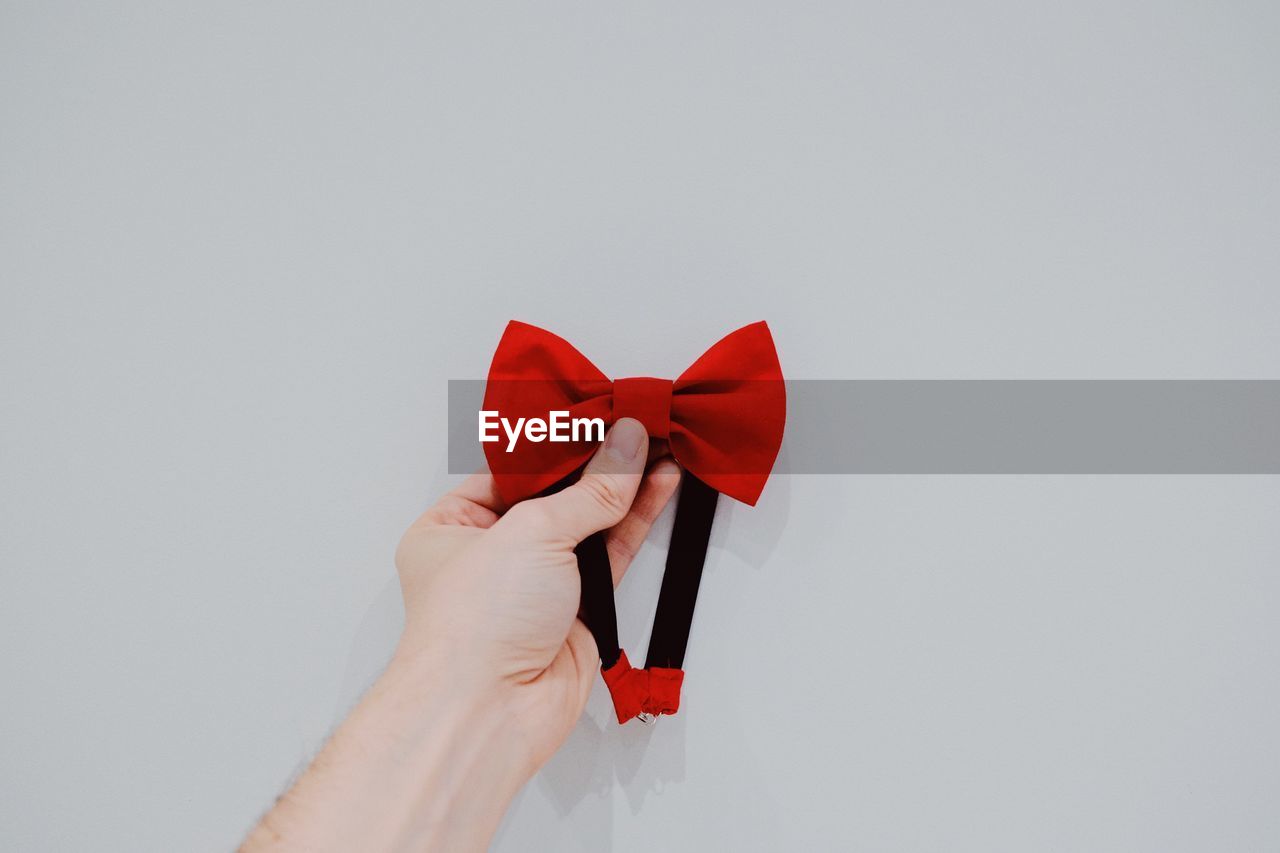 Close-up of hand holding red bowtie over white background