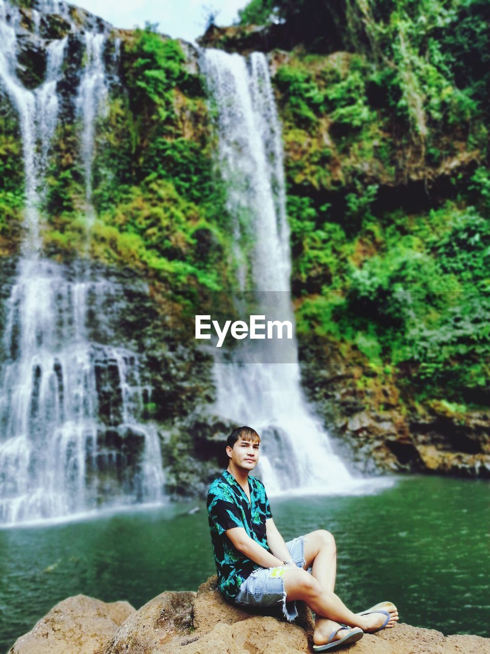 Man sitting on rock against waterfall in forest