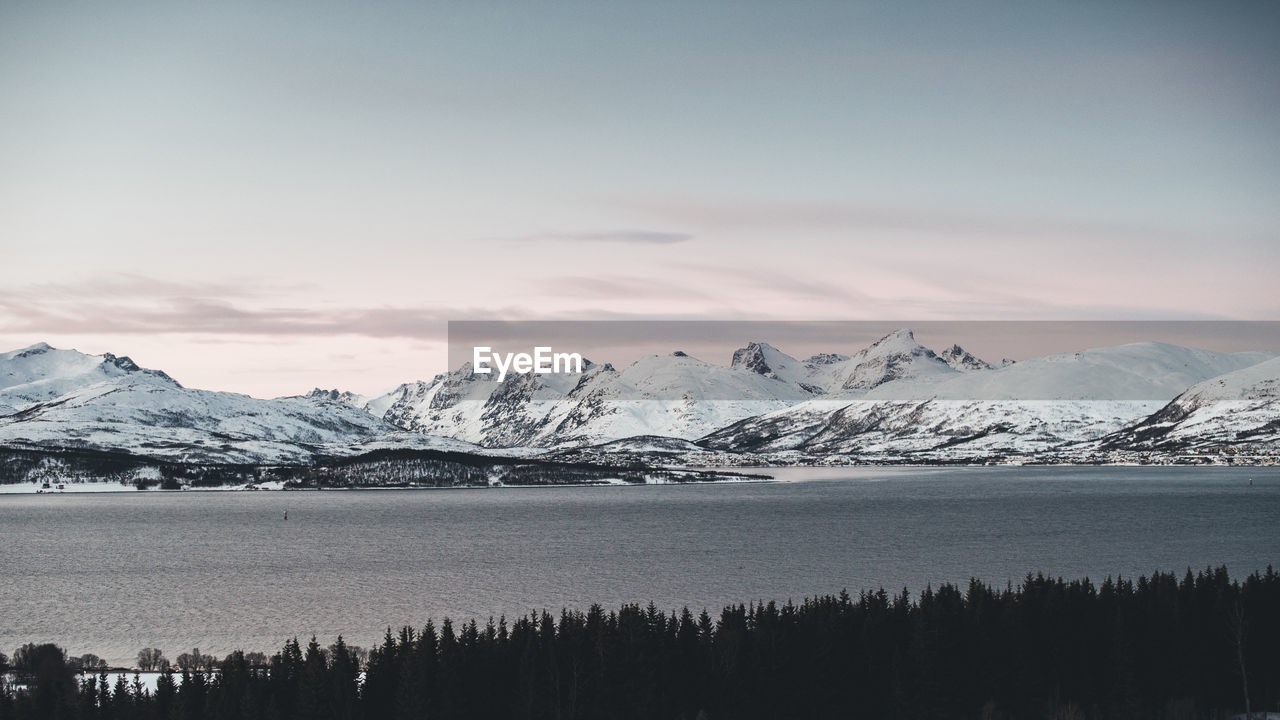 Scenic view of lake against snowcapped mountains during sunset