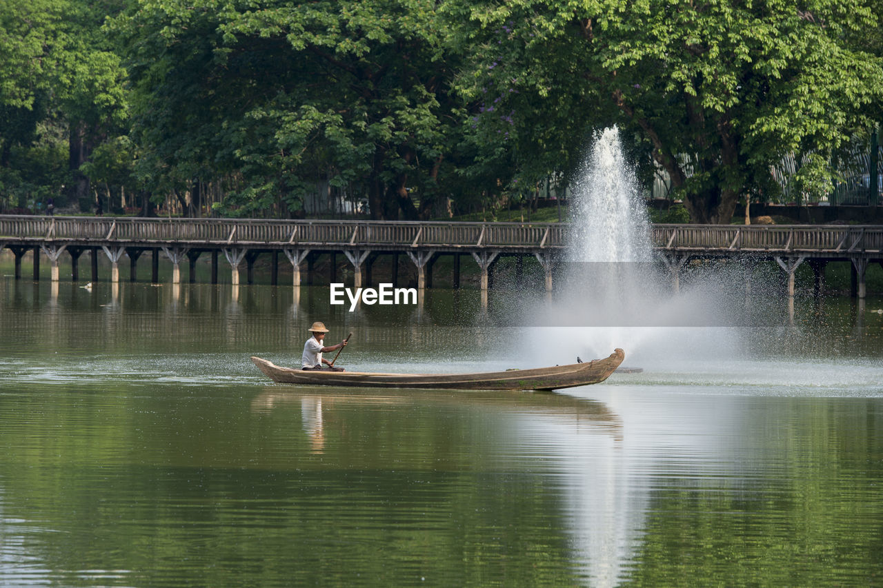 Man oaring boat by fountain on river