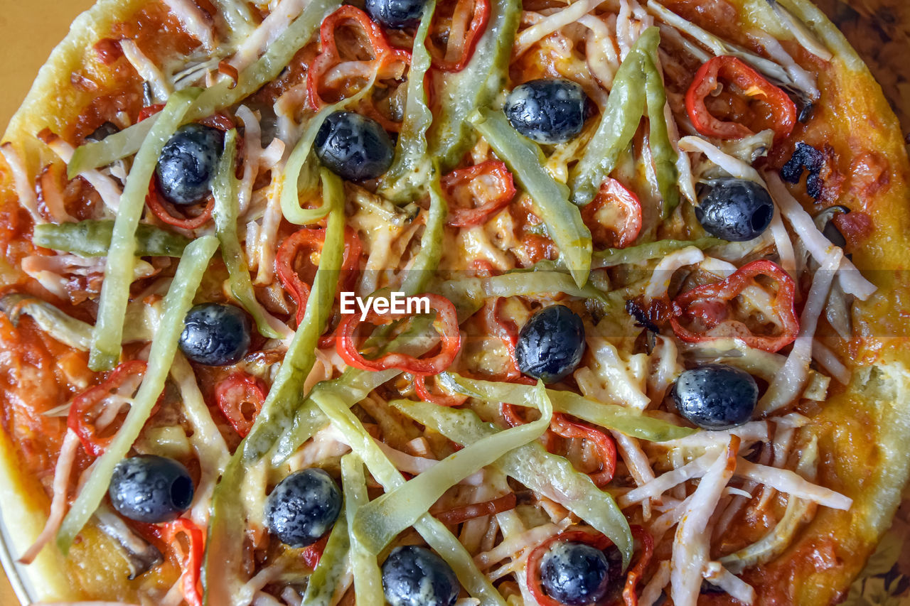 Freshly prepared italian pizza - olives, ham, pepper, sauce, cucumber, cheese. top view