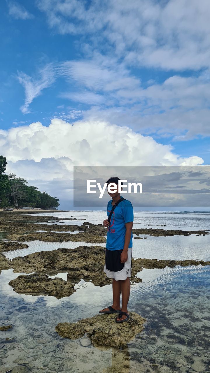 Full length of man standing on rock at beach against sky