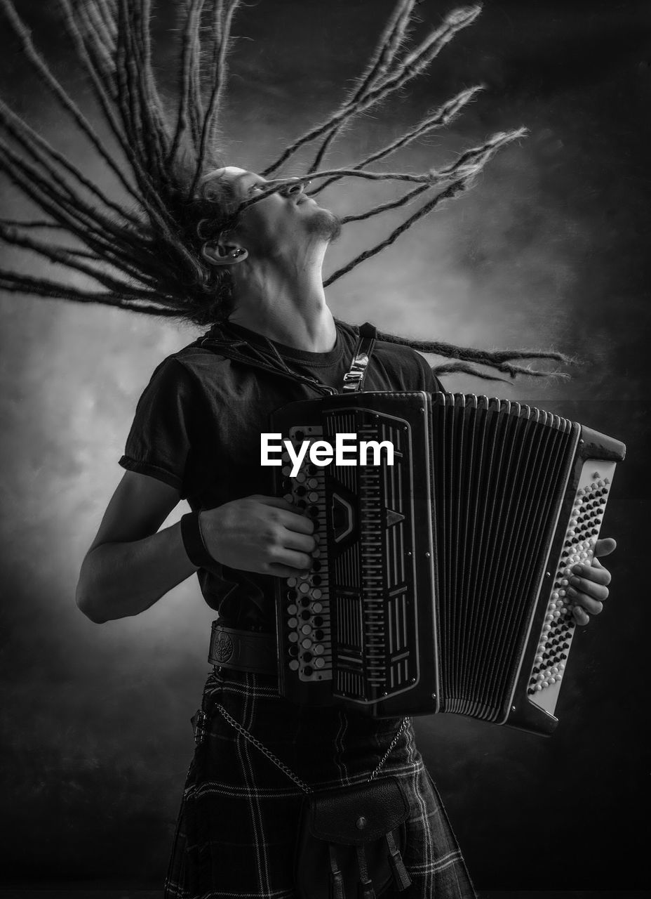 Man playing accordion while tossing dreadlocks