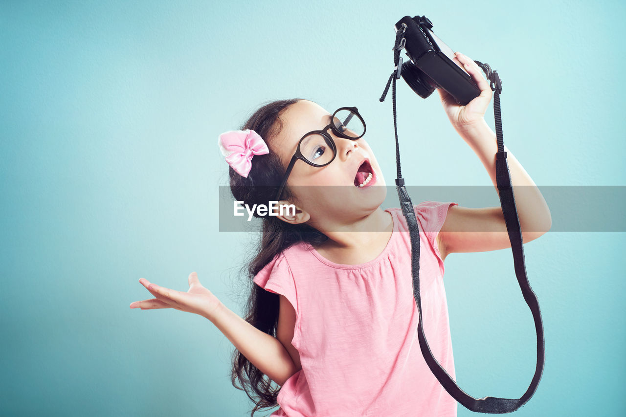 Girl taking selfie with camera while standing against turquoise background