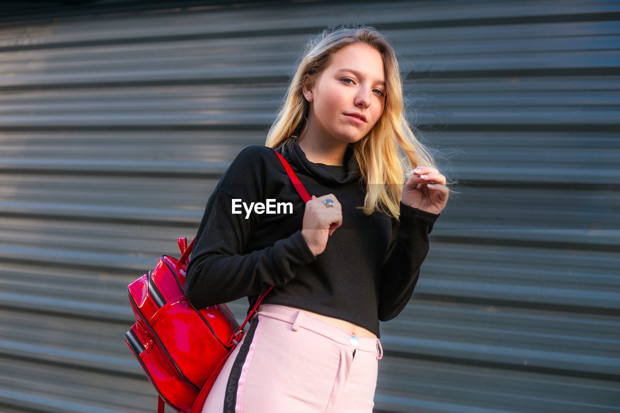 Young blond hair woman carrying a backpack. blond hair girl walking on the street with backpack.