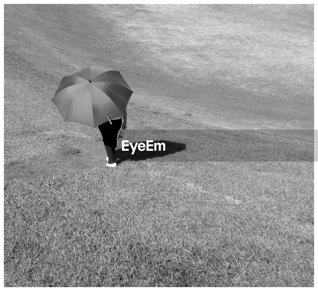 Person with umbrella walking on grassy field