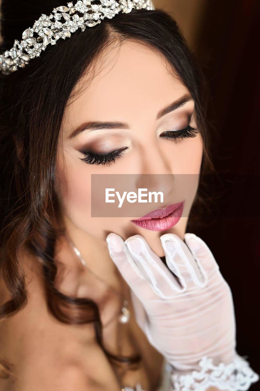 Beautiful young bride with hand on chin against brown background