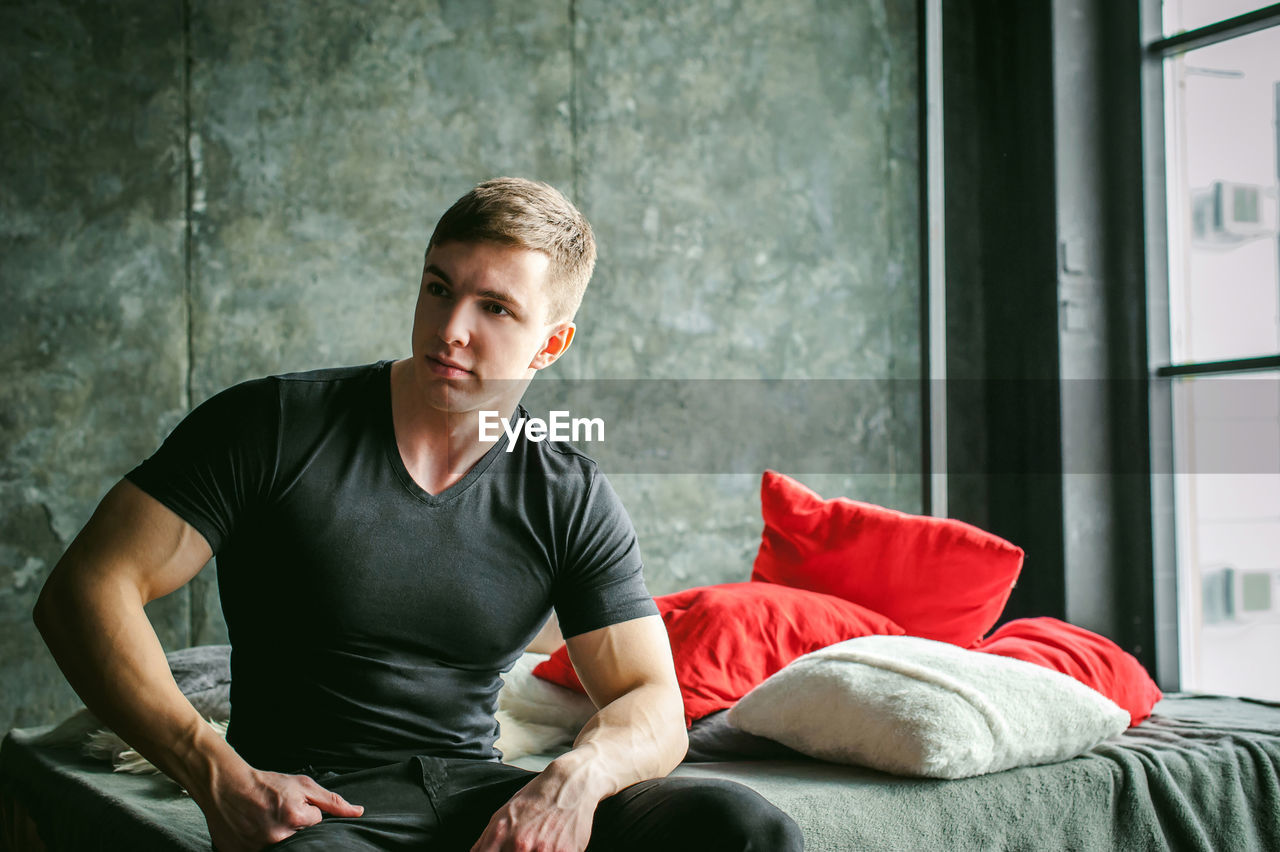 Muscular man sitting on bed at home