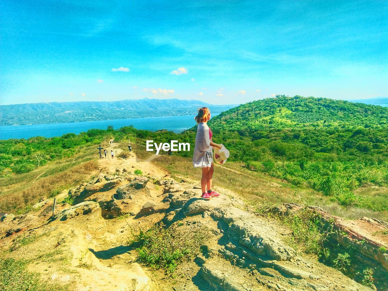 Side view of young woman standing on mountain against sky during sunny day