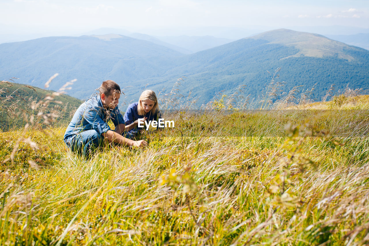 Couple crouching on grass against mountain