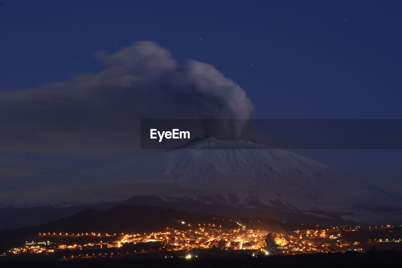 Aerial view of illuminated cityscape against sky at night and etna eruption