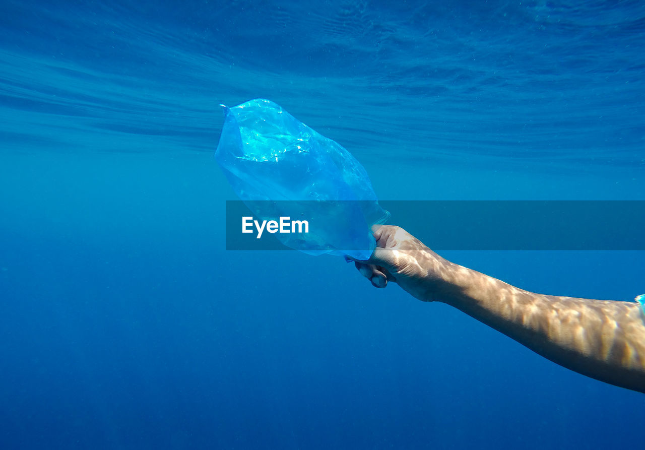 Cropped hand holding plastic bag in sea