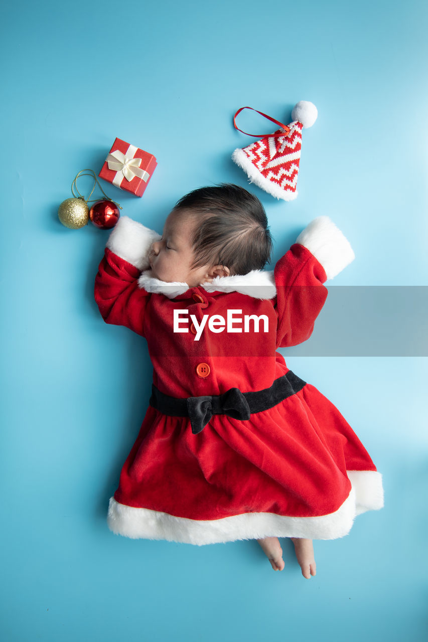 Directly above shot of baby girl wearing santa claus costume sleeping on blue background