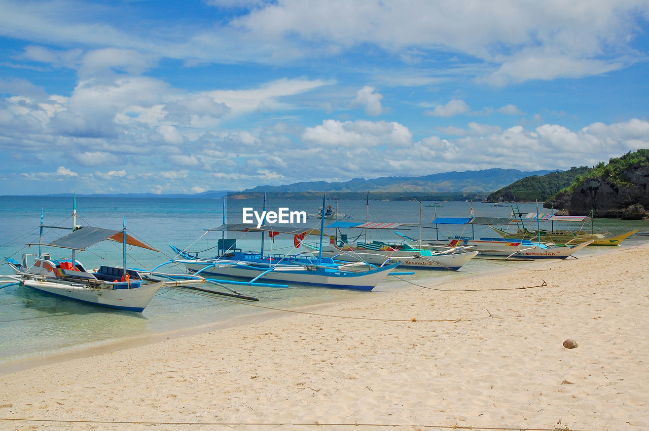 BOATS MOORED ON SHORE AGAINST SKY