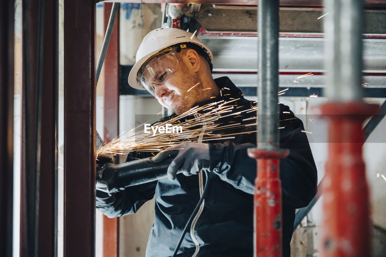 Male construction worker cutting metal with machinery at site