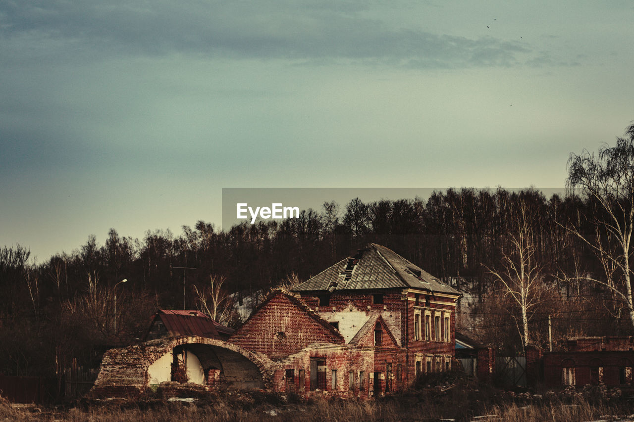 Old house on field by trees against sky