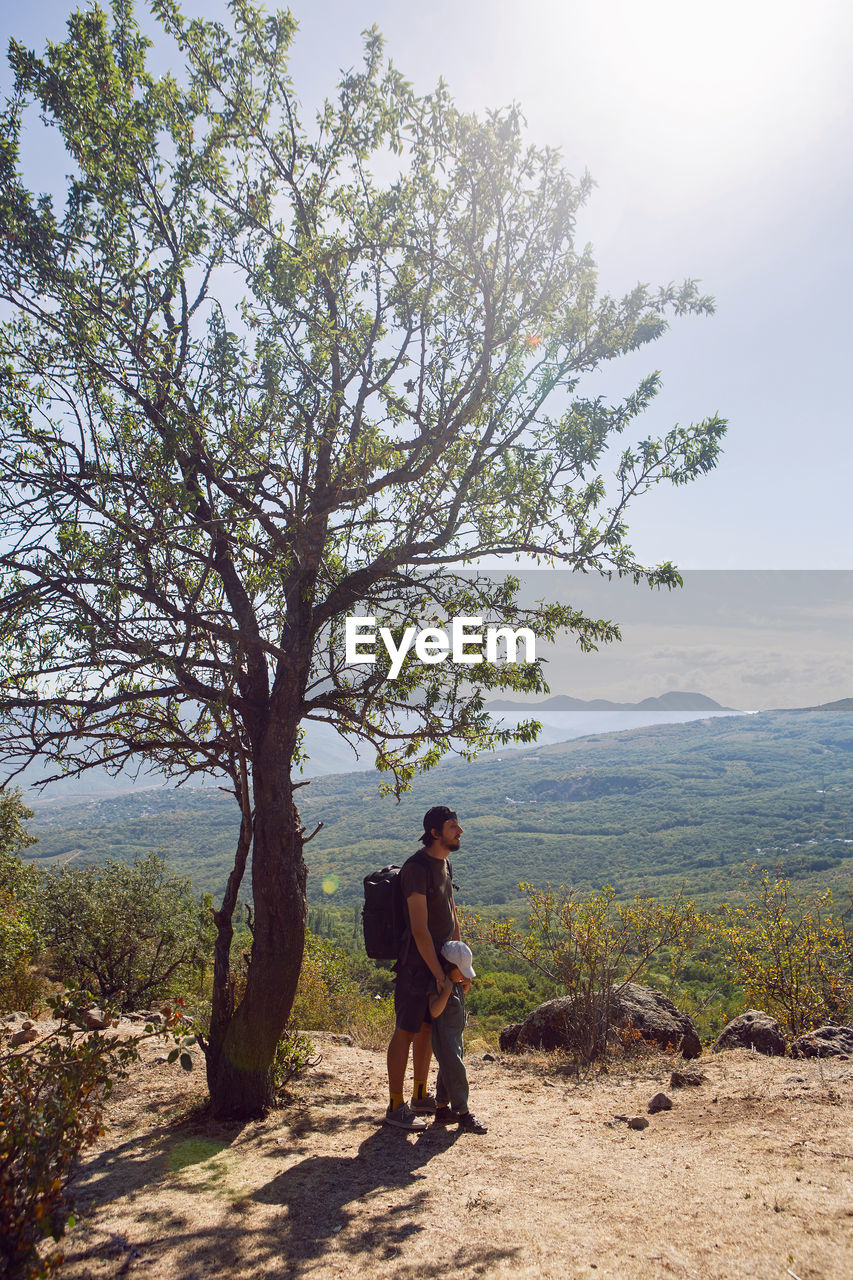 Father with a backpack and his son stands next to a tree on a mountain in the summer in the crimea